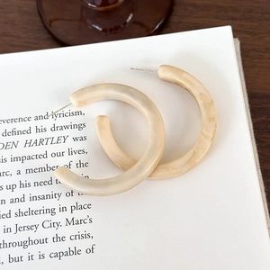 Dettaglio di orecchini a cerchio a forma di C in resina marmorizzata beige su un libro