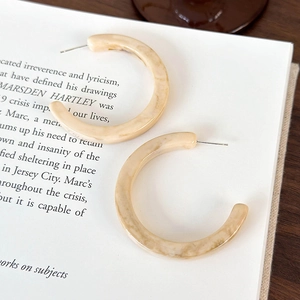 Dettaglio degli orecchini a cerchio a C in resina marmorizzata su sfondo di libro
