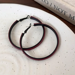 Detailed close-up of oversized burgundy leather-wrapped hoop earrings on a ceramic tray