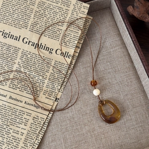 Vue détaillée du pendentif en résine ambrée avec perle vintage et cordon marron