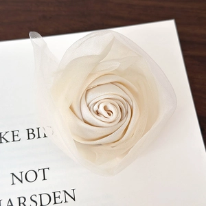 Detailansicht einer creme-satinierten Tüll-Rosen-Haarklammer auf einem Buch