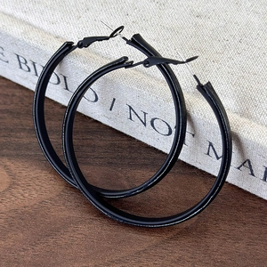 Close-up of minimalist large matte black hoop earrings on a textured wooden background