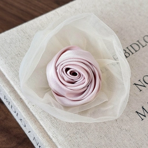 Nahaufnahme einer rosa Satinrose mit elfenbeinfarbenem Netz auf einem Leinenbuch