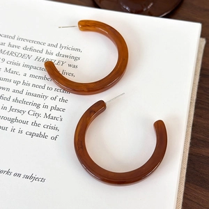 Dettaglio di orecchini a cerchio a C in ambra tartarugata su pagine di libri vintage