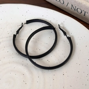 Close-up of matte black leather-wrapped hoop earrings on white ceramic plate