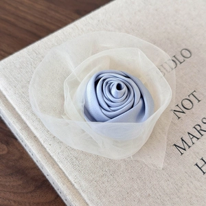 Detail einer blauen Satin-Rosen-Haarklammer mit cremefarbenen Netzelementen auf Buch