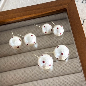 Close-up of three pairs of cream cotton pearl stud earrings with red polka dots on a tray