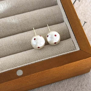 Detail view of red polka dot pearl studs in a luxury jewelry box with golden posts