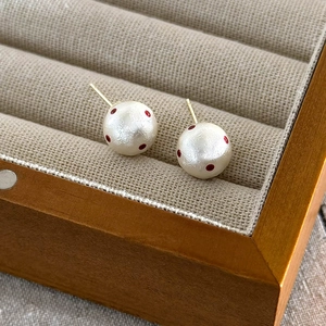 Detailed close-up of red polka dot cotton pearl earrings in a wooden jewelry box