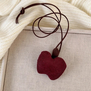 Close-up of a handmade red corduroy apple pendant necklace with adjustable leather cord