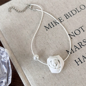 Detail of white rose and pearl charm necklace on rustic burlap book background