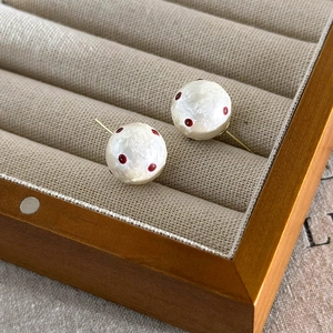 Detailed close-up of French-style red polka dot cotton pearl earrings in a wooden box