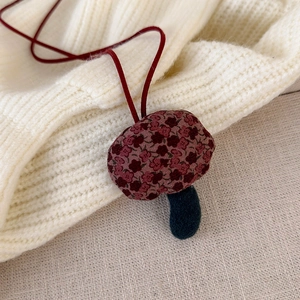 Close-up of handmade fabric mushroom pendant on a soft beige knitted sweater