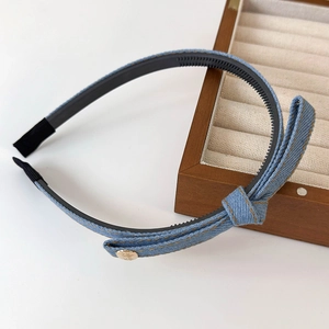 Detail view of denim headband with bow and gold button on a white background