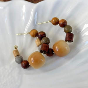 Detail of bohemian C-shaped earrings with wooden beads and resin stone on a white tray