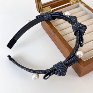Detail of blue denim headband with bow and pearls on a wooden jewelry display case