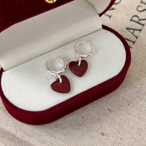 Elegant silver hoop earrings with dark red heart pendants on a red velvet jewelry box