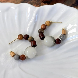 Close-up of ethnic C-shaped earrings with sandalwood and stone beads on a ceramic tray
