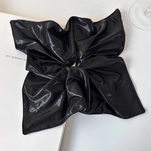 Macro view of shiny black oversized scrunchie with silky pleated fabric texture