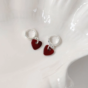 Macro shot of polished silver hoop earrings with deep red heart pendants on a tray