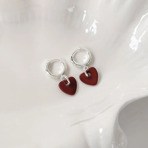 Detailed view of silver hoop earrings with deep red heart pendants on a shell tray