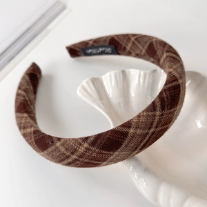 Macro view of a brown plaid headband placed on a white shell-shaped ceramic plate