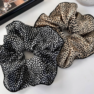 Detailed view of two leopard print scrunchies in black-white and khaki-black satin fabric