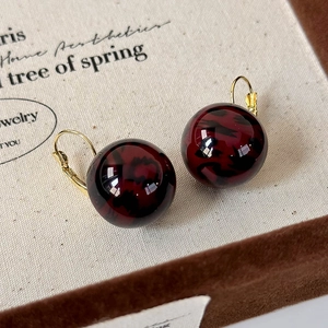 Detailed shot of dark red marble leopard print ball earrings with golden lever-back hooks
