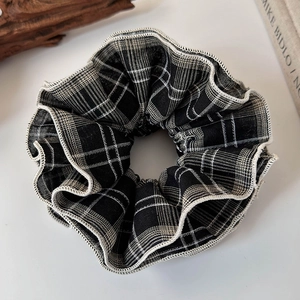 Close-up of black and white plaid scrunchie with ruffled lace edge on white background