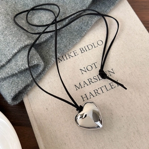 Collier minimaliste avec grand pendentif cœur argenté et cordon noir sur fond texturé