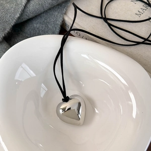 Collier cœur argenté minimaliste avec cordon noir dans un bol en céramique blanche