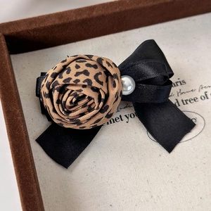 Détail de la pince à cheveux avec rose léopard, nœud en ruban noir et perle élégante