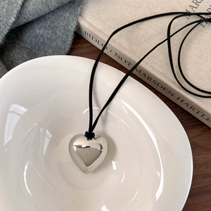 Collier minimaliste avec pendentif cœur argenté et cordon noir dans un bol blanc