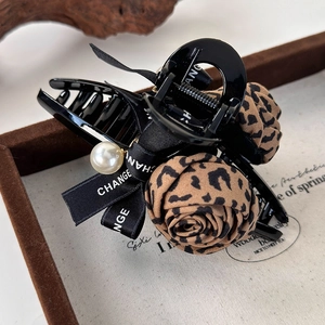 Détail de roses en tissu léopard et d'une perle blanche sur une pince à cheveux noire