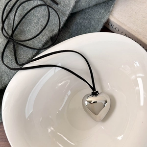 Gros plan d'un pendentif coeur argenté avec cordon en daim noir dans un bol en céramique