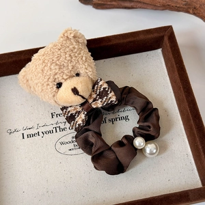 Détail d'un chouchou ours en peluche avec nœud à carreaux marron et perles décoratives