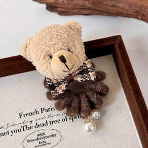 Détail d'un chouchou ours en peluche avec élastique marron et pendentifs en perles