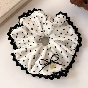 Detailed close-up of white velvet polka dot hair scrunchie with black lace trim and golden charm