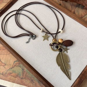 Detail of vintage bronze feather pendant with wooden beads and starfish charms on a cord necklace