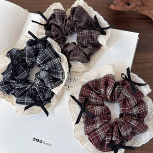 Three retro plaid hair scrunchies with lace edges and bows on a book background