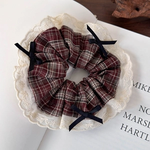 Detailed view of red plaid scrunchie with white lace edges and small black bow accents