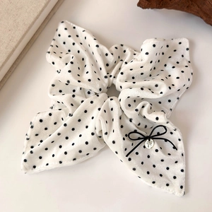 Detailed macro view of white velvet polka dot hair scrunchie with bow and gold charm detail