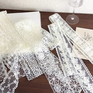 Detail of vintage white lace ribbon featuring intricate floral embroidery on dark wood
