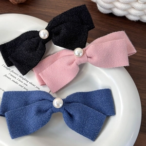 Drei elegante Schleifen-Haarspangen mit Perlen in Schwarz, Rosa und Blau auf Keramik