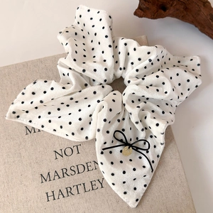 Detail view of white velvet hair scrunchie with black dots, lace trim, and bow tie