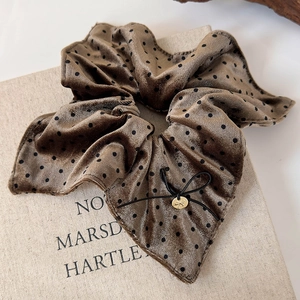 Macro view of brown velvet polka dot scrunchie with a black bow and gold charm detail
