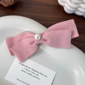 Detail einer Haarspange mit rosa Stoffschleife und Perle auf einem weißen Teller