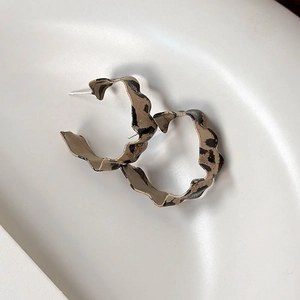 Detail of leopard print resin hoop earrings with irregular wavy edges and silver pins