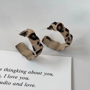 Detail of leopard print C-shape earrings with irregular wavy texture on grey backdrop
