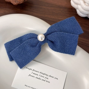 Detailansicht einer blauen Schleifen-Haarspange mit Perle auf einem Keramikteller
